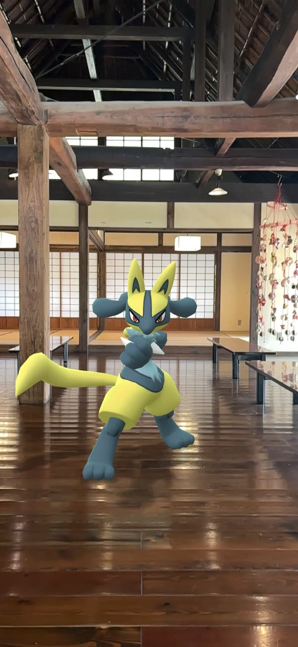A yellow and black Pokémon character posing on a polished wooden floor inside a traditional Japanese hall with timber beams and paper screens.